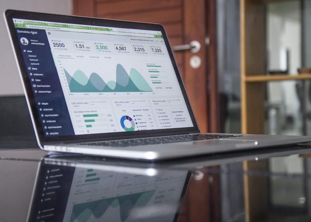 A laptop on a reflective surface showing different chart types for data visualization in business.